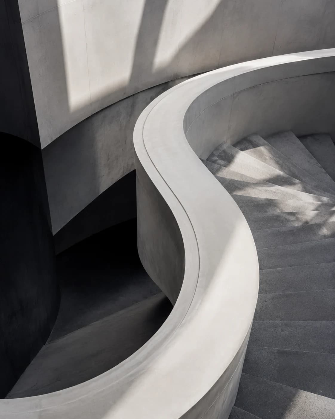 Skulpturale Betontreppe mit geschwungener heller Brüstung, mineralischen Oberflächen und präzisem Licht- und Schattenspiel.
